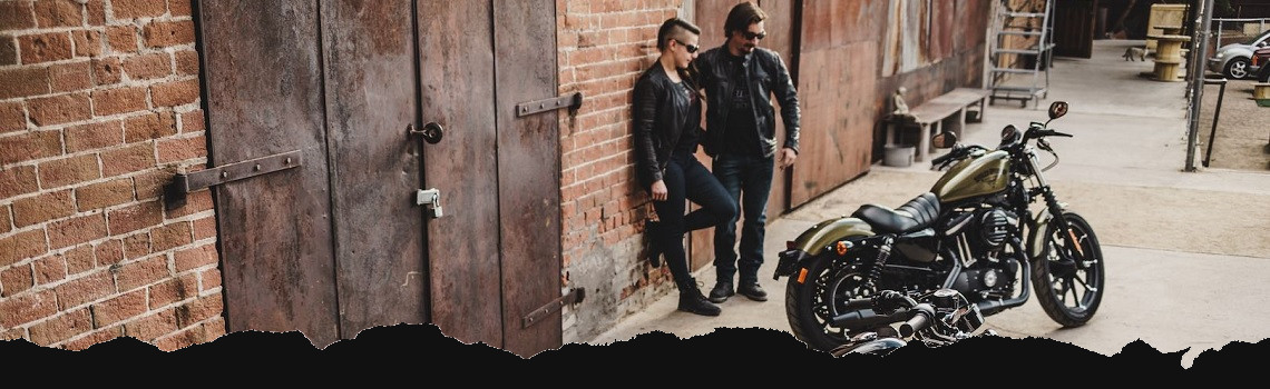 A couple taking a riding break outside of a brick building next to a Harley® motorcycle.